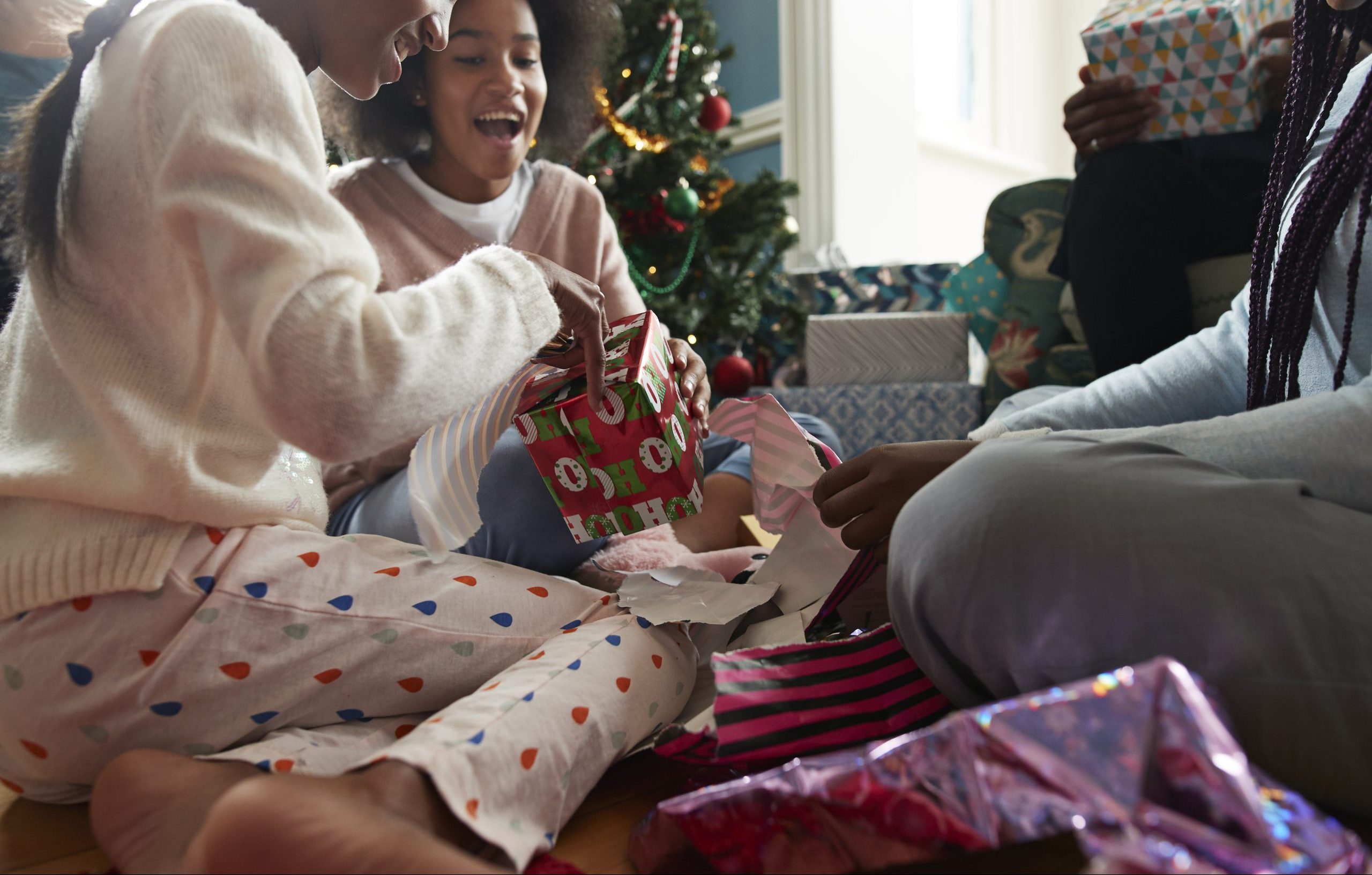 Happy sisters opening Christmas presents while sitting in living room at home