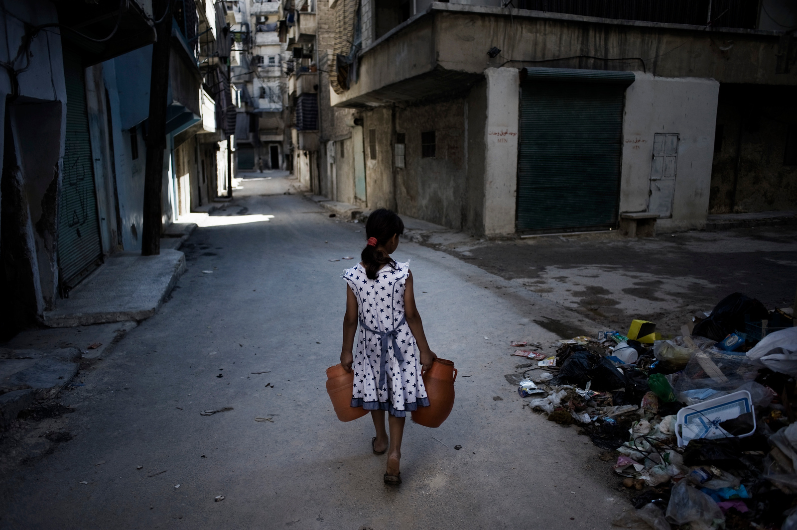 A girl carrying jerry cans of water walks past a pile of debris on a street in Aleppo in 2012. Access to water has only worsened as Syria’s war grinds on.