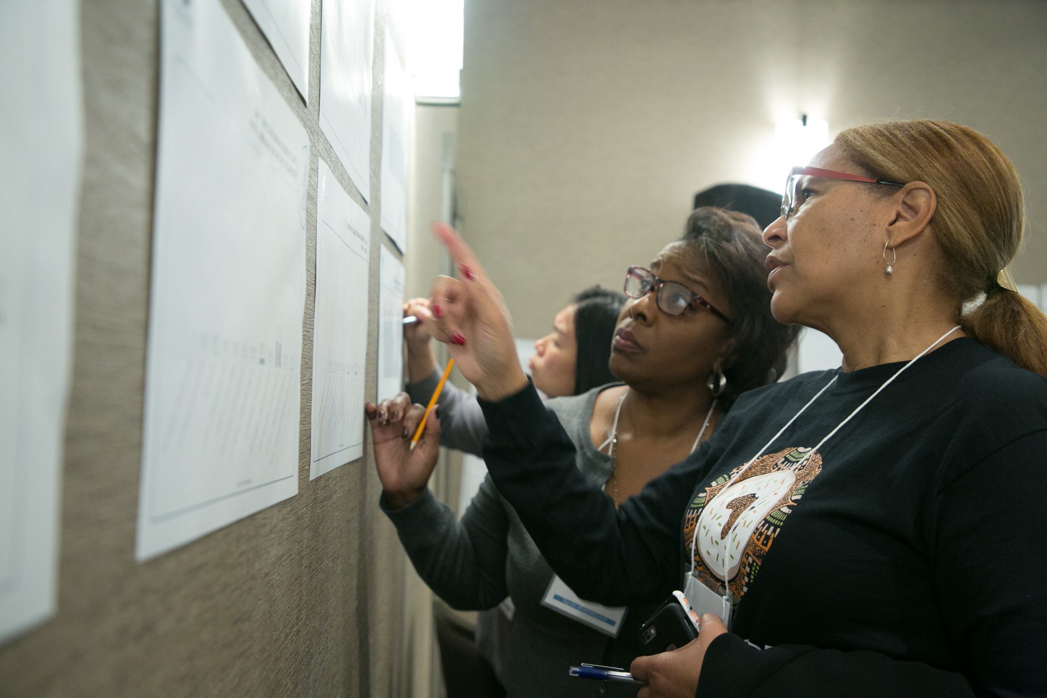 Four people are writing on sheets of paper attached to a wall.