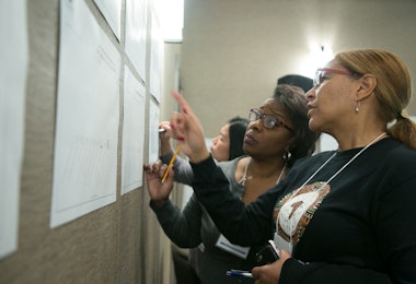 Four people are writing on sheets of paper attached to a wall.