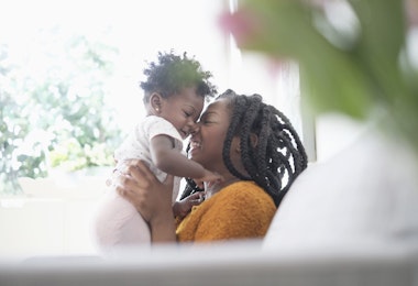Black woman rubbing noses with baby daughter on sofa