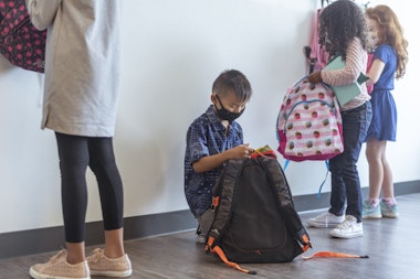 Elementary age students wearing protective face masks put their backpacks away in their classroom when arriving at school during the COVID-19 pandemic