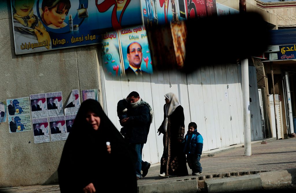 Iraqis walk on the street in Baghdad, on election day, January 31, 2009, as a campaign poster of Prime Minister Nouri al-Maliki is seen in a car rearview mirror. Source: Chris Hondros/Getty Images