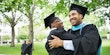 Two Black students in graduation robes embracing.