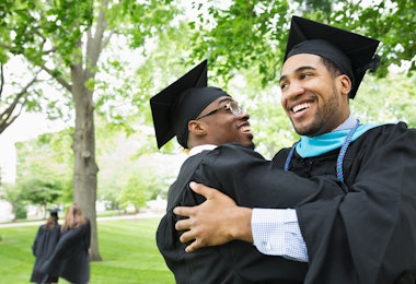 Two Black students in graduation robes embracing.