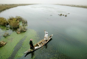 AL-FOHUD, IRAQ - JUNE 3: A Marsh Arab guides his boat through a marsh area that is slowly being re-flooded with water June 3, 2003 in Al-Fohud, Iraq. The Marsh Arabs have inhabited the swamplands in the area for approximately 5,000 years, but their lifestyle was virtually destroyed by Saddam Hussein following the 1991 Shiite uprising in the region. Hussein constructed dams and diverted waterways to drain the marshes in an effort to destroy the Marsh Arabs. Following the war, some dams have been re-opened allowing the marshes to slowly begin to refill and some Marsh Arabs are beginning to return to their old lifestyle. (Photo by Mario Tama/Getty Images)