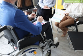 A close-up shot of a man in a wheelchair holding documents and speaking with coworkers.