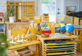 A Montessori classroom set-up complete with desks, paint racks, globes, musical instruments, plants, writing utensils, and other education inspiring tools.