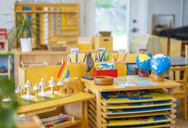 A Montessori classroom set-up complete with desks, paint racks, globes, musical instruments, plants, writing utensils, and other education inspiring tools.