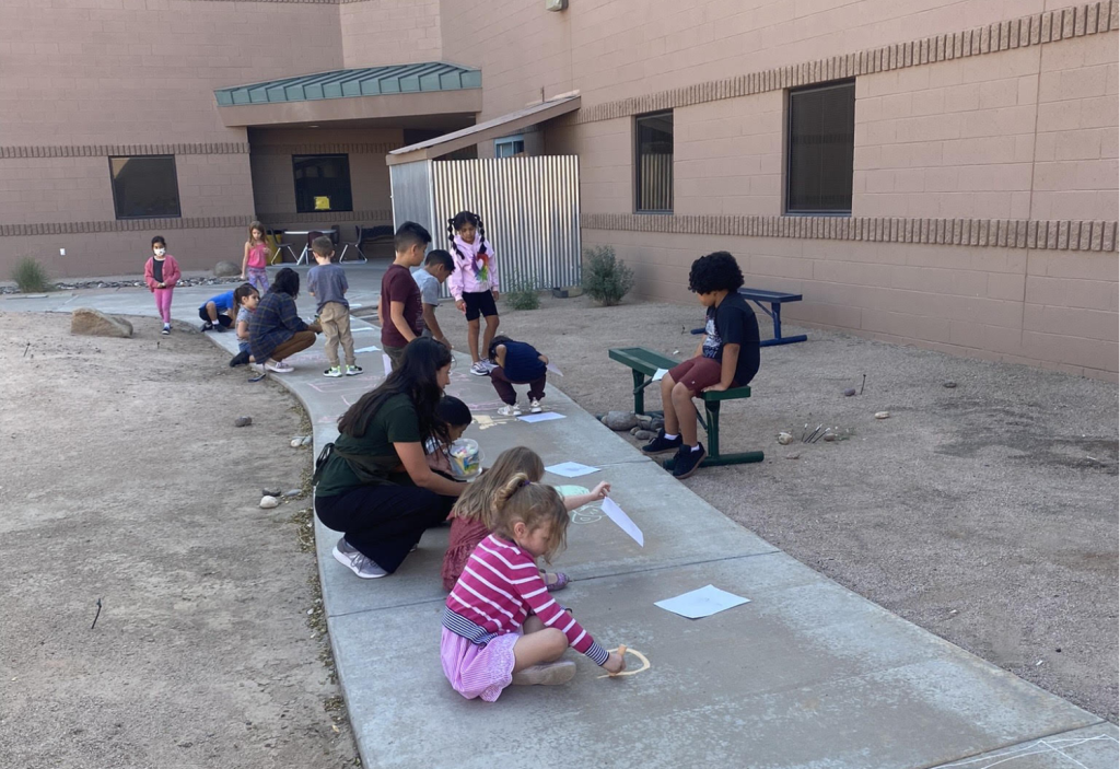 Students outside of a school building drawing on a cement pathway.