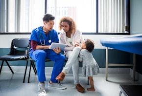 A nurse showing digital tablet to mother and child in a hospital.