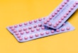 Two blister packs of contraceptive pills on a yellow background.