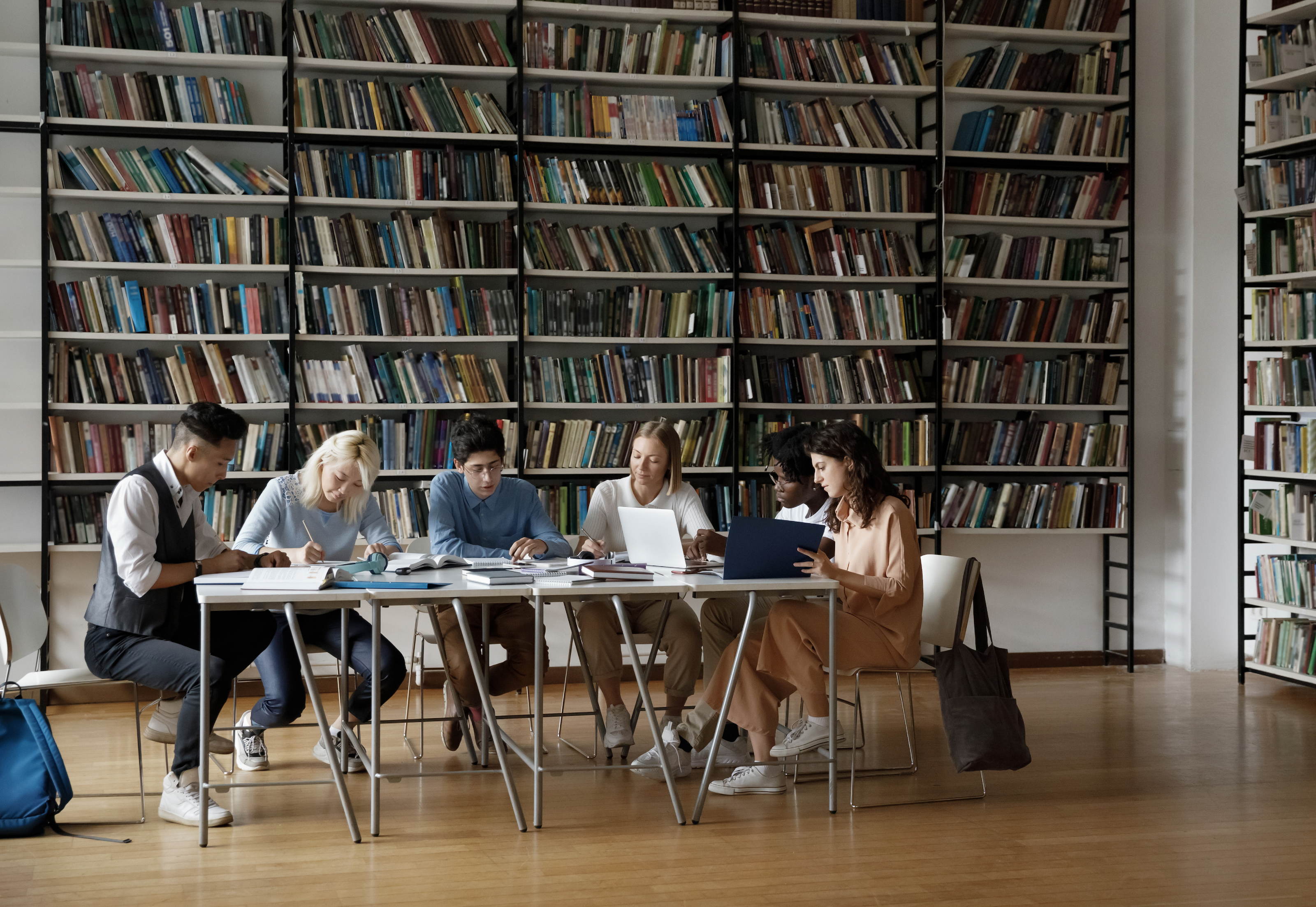 A group of students sitting at a table surrounded by bookcases.