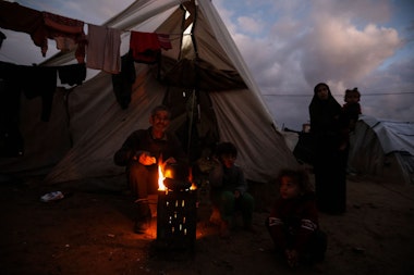 RAFAH, GAZA - JANUARY 23: Displaced Palestinians keep warm by a fire near their tent on January 23, 2024 in Rafah, Gaza. The toll since the Oct. 7 war in Gaza between Israel and Hamas now exceeds 25,000 dead and 62,000 injured, according to the territory's health ministry. Two-thirds of the victims are believed to be women and children. The United Nations estimates for its part that more than 18,000 Palestinian children have lost a parent. With 25 per cent of the population, or more than half a million people, are in a situation of 