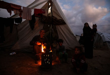 RAFAH, GAZA - JANUARY 23: Displaced Palestinians keep warm by a fire near their tent on January 23, 2024 in Rafah, Gaza. The toll since the Oct. 7 war in Gaza between Israel and Hamas now exceeds 25,000 dead and 62,000 injured, according to the territory's health ministry. Two-thirds of the victims are believed to be women and children. The United Nations estimates for its part that more than 18,000 Palestinian children have lost a parent. With 25 per cent of the population, or more than half a million people, are in a situation of 