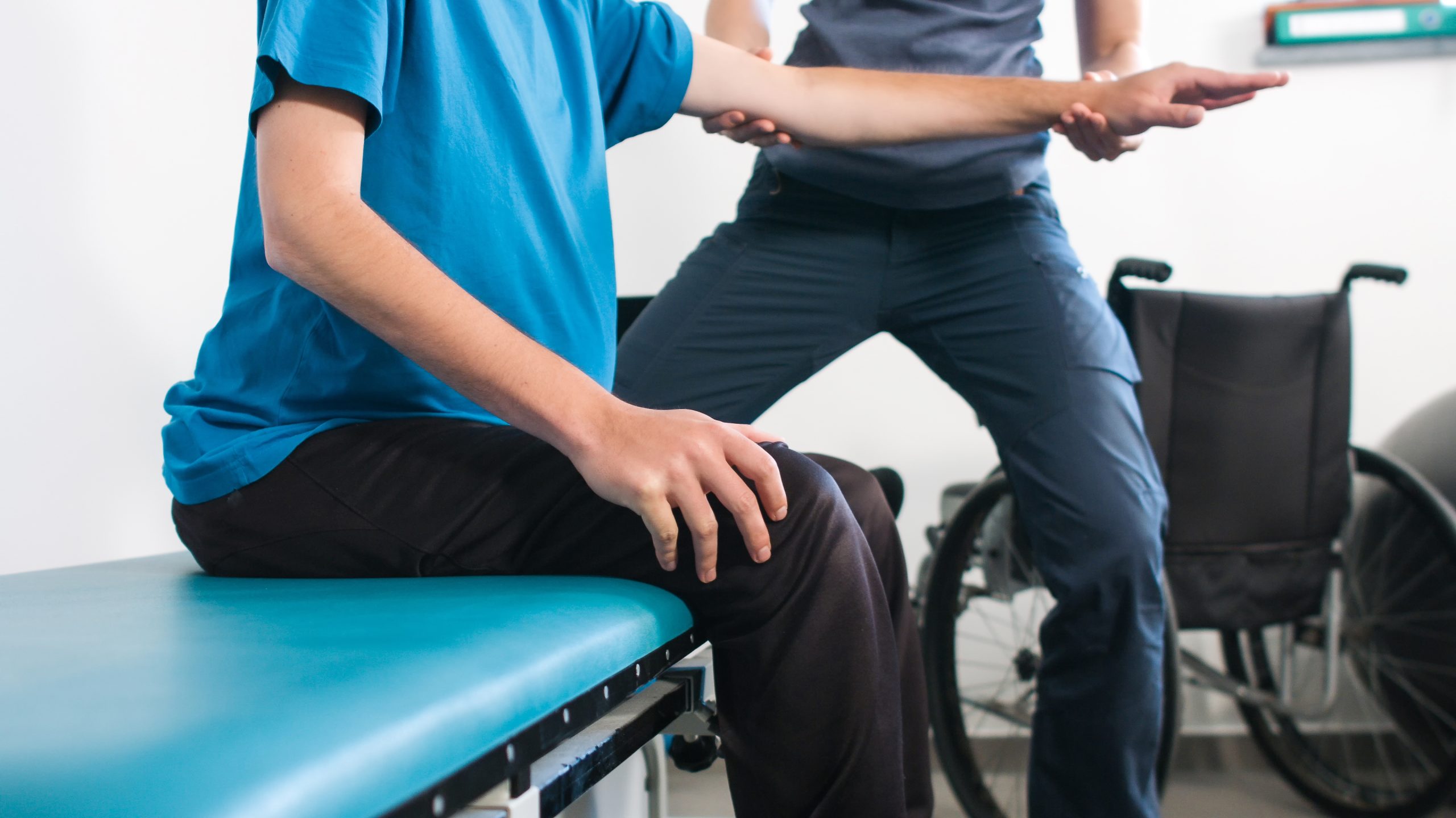 Physiotherapist exercising with disabled person using wheelchair on a therapy table.