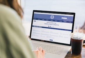 An over the shoulder photo of an unrecognizable woman applying for unemployment benefits.  She is using the government website.