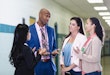 A multiracial group of four teachers or school administrators having a discussion in a school corridor. An African-American man wearing a full suit is talking with three female coworkers. Perhaps he is the school principal.