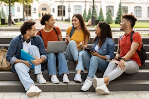 College Lifestyle. Group Of Students Relaxing Together Outdoors, Sitting On Stairs In Campus Park, Cheerful Millennial Men And Women Chatting And Laughing, Multiethnic Friends Resting After Classes