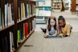 Two young girls reading a book on the floor of library