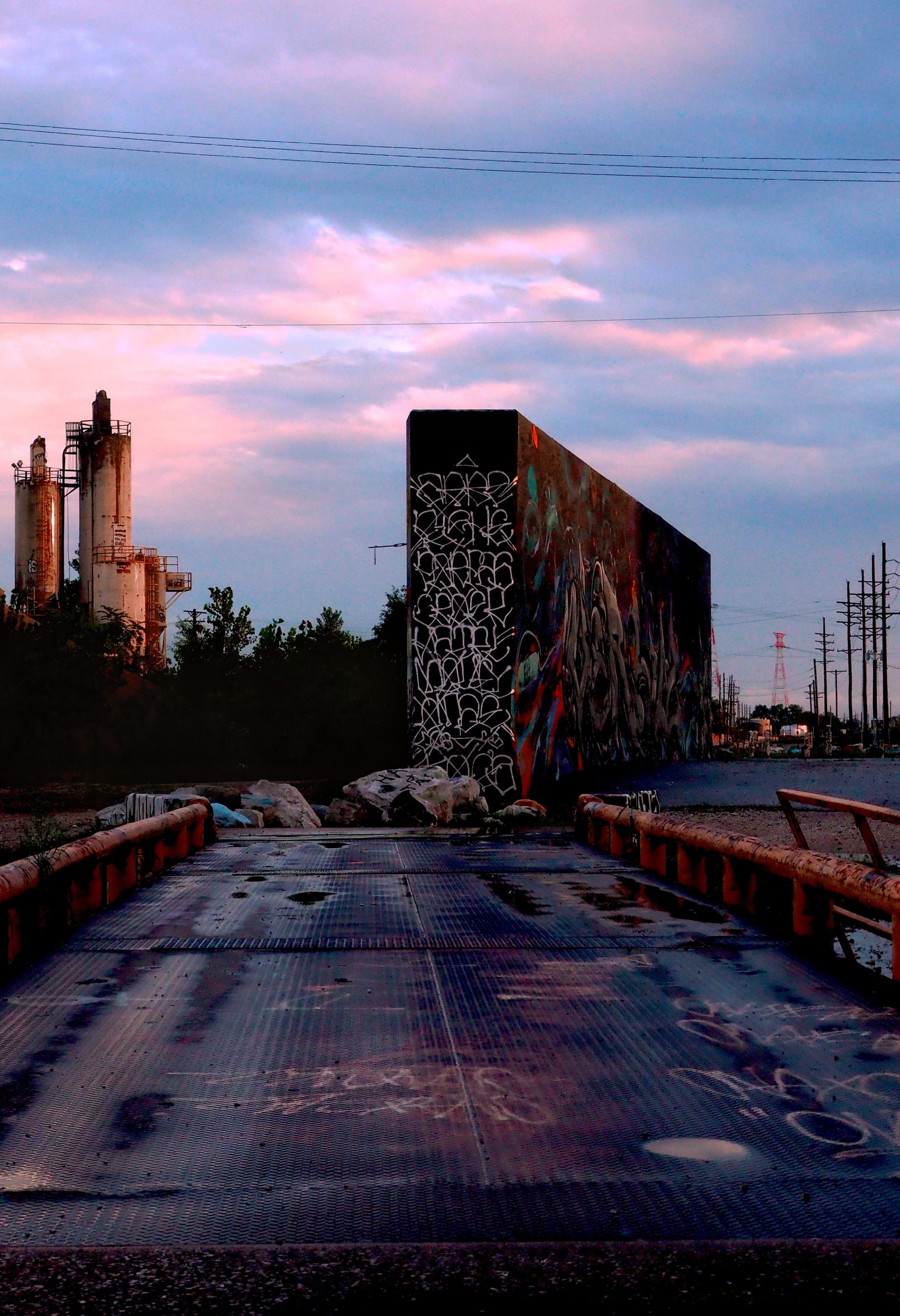 A photograph of a cement wall covered in graffiti, set against a pink and purple sunset