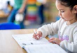 A sweet mixed race elementary student sits at her desk as she works through a writing workbook independently.