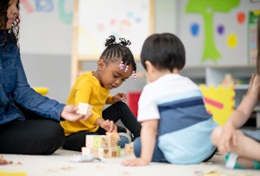 A diverse group of kids sit on the carpet and play with each other.