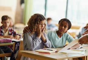 Displeased schoolgirl feeling shocked while looking at her bad exam results and her black friend is consoling her.