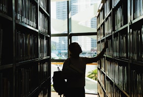 female student in silhouette looking at the books from the bookshelf
