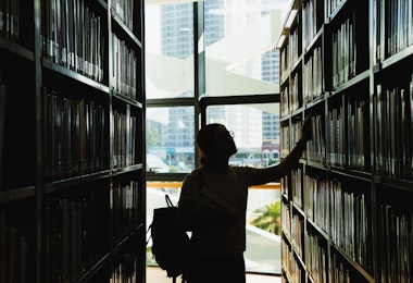 female student in silhouette looking at the books from the bookshelf