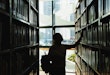 female student in silhouette looking at the books from the bookshelf