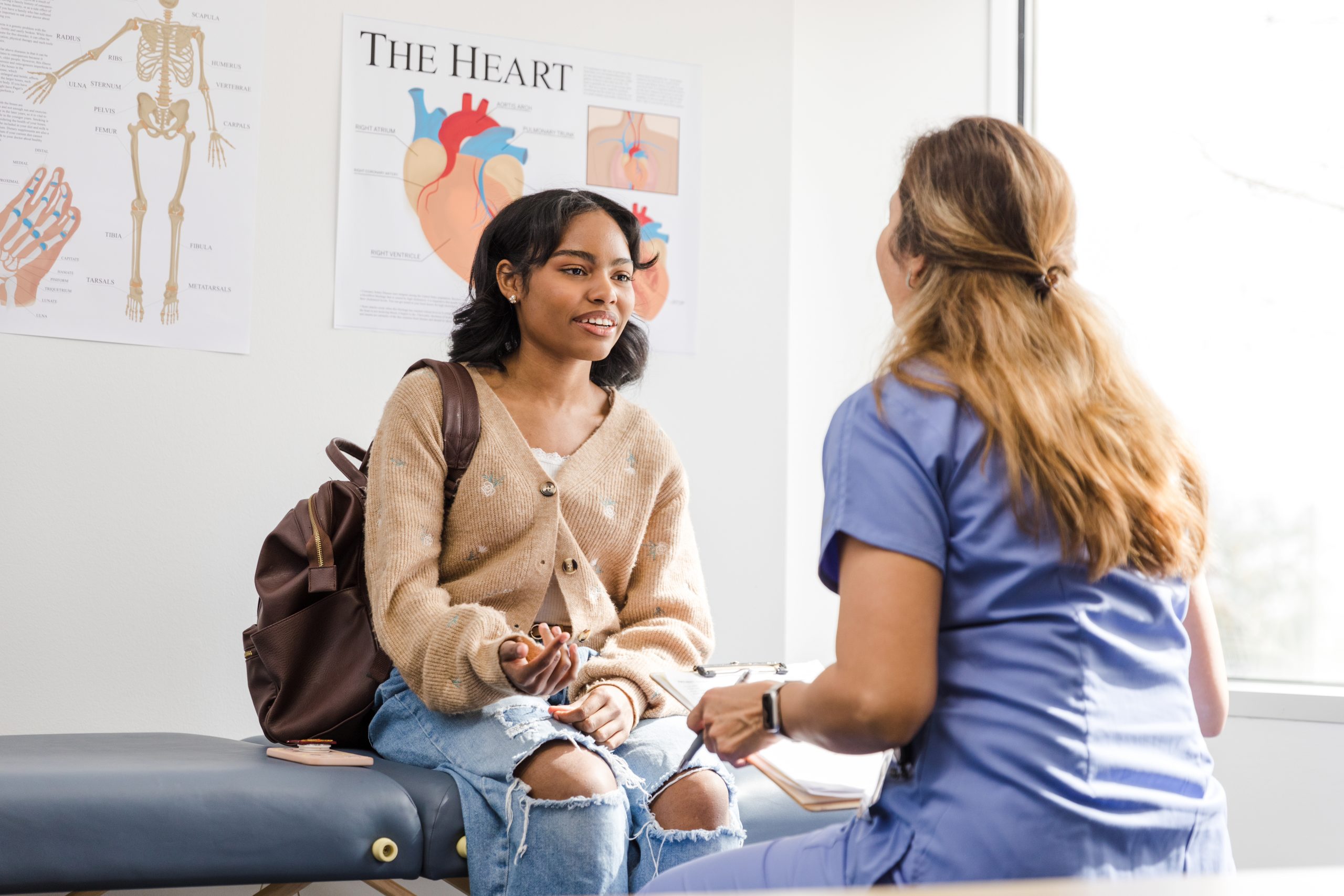 The teenage girl gestures as she shares her symptoms with the unrecognizable female doctor.