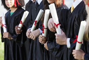 Cropped view of multi-ethnic friends graduating together, in cap and gown. Shallow DOF. focus on girl in middle.