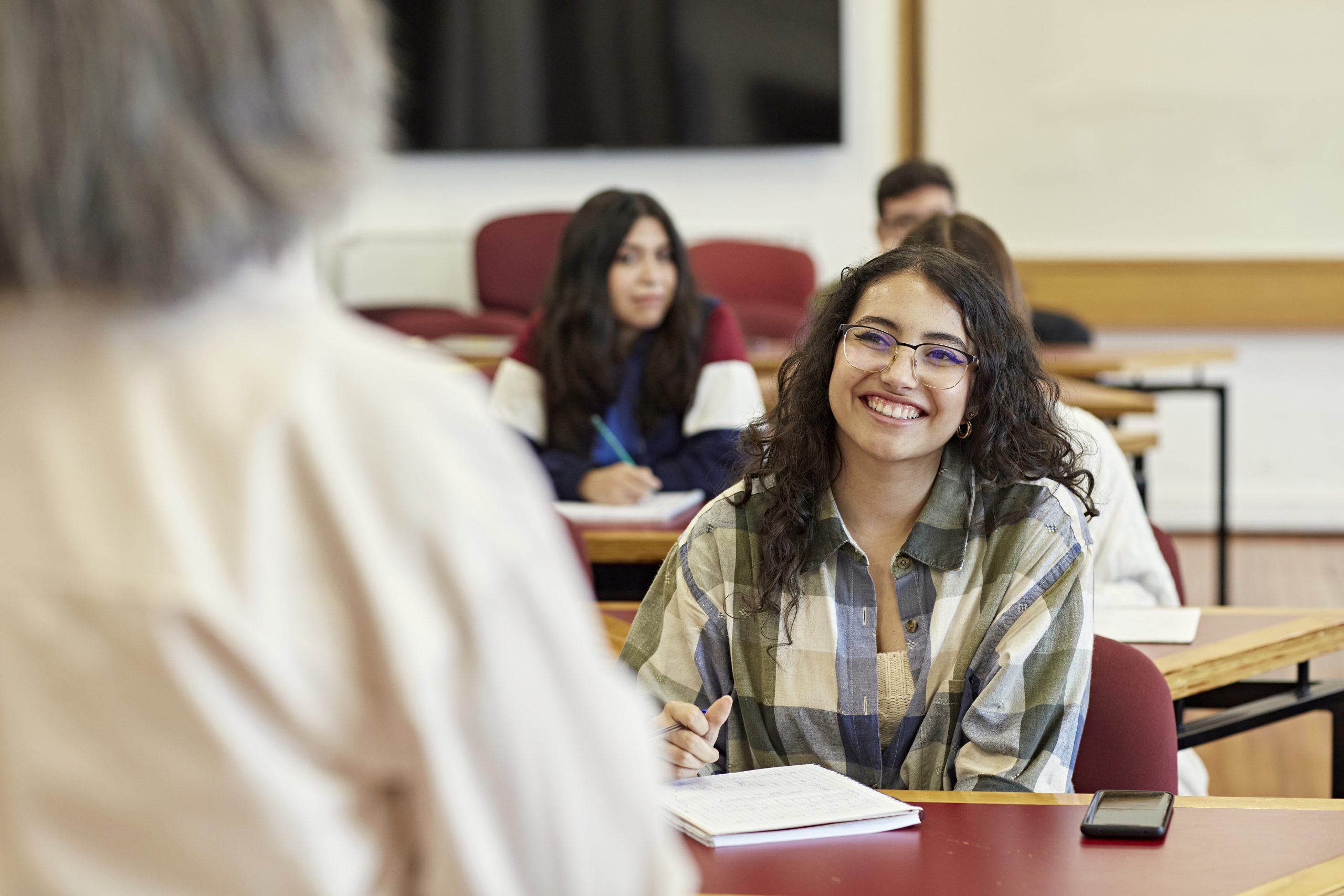 Over the shoulder view with focus on young woman sitting in front row of college classroom, enjoying the lecture and taking notes. Property release attached.