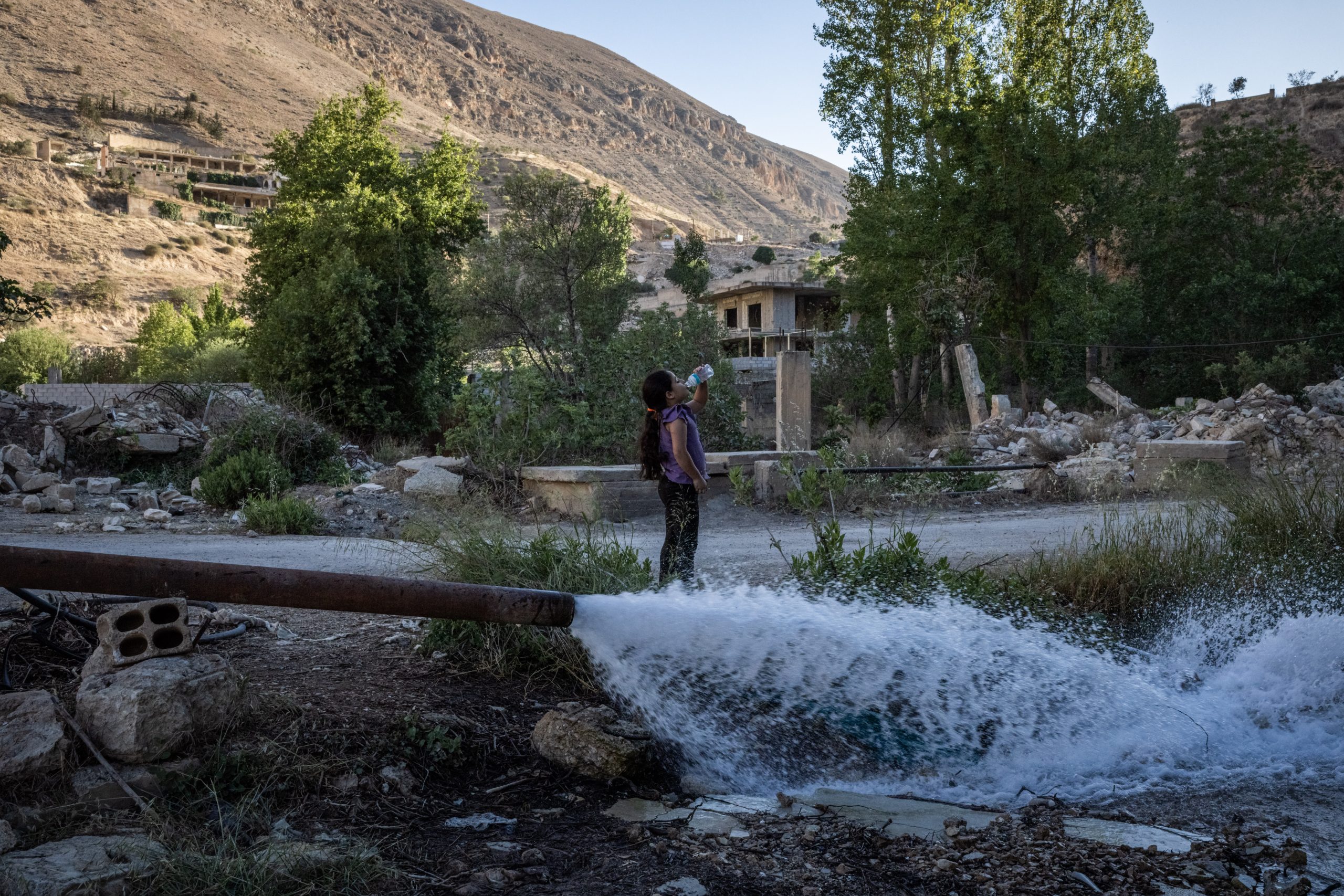 DAMASCUS, SYRIA - MAY 28: A girl fils a water bottle to drink from a pipe spraying water near the site of a spring that has been used since roman times on May 28, 2025 in Damascus, Syria. The Barada Valley, the main water source for Damascus, is depleted this year after one of the driest winters in decades. (Photo by Ed Ram/Getty Images)