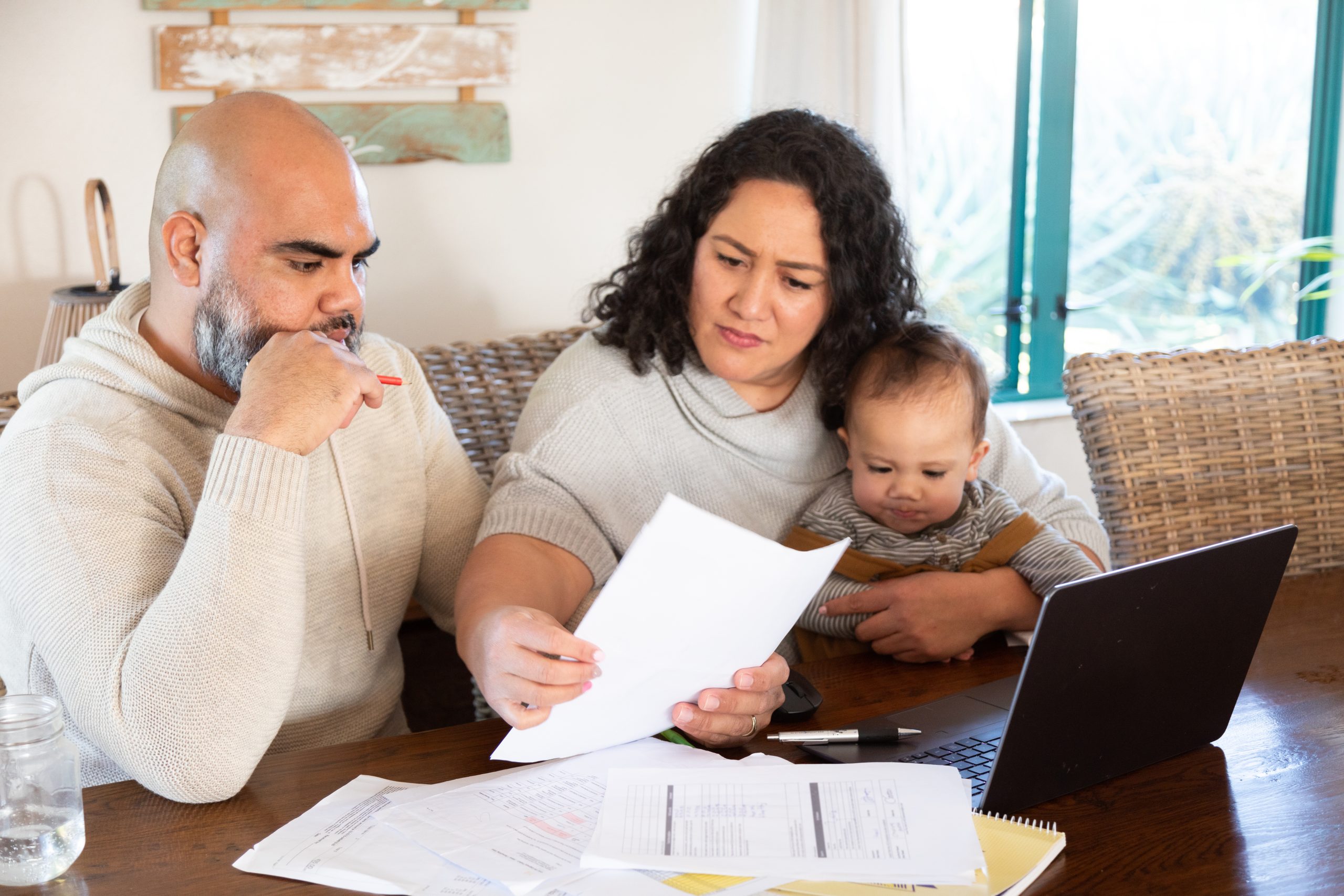 a couple with baby look at accounts and laptop at kitchen table