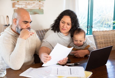 a couple with baby look at accounts and laptop at kitchen table