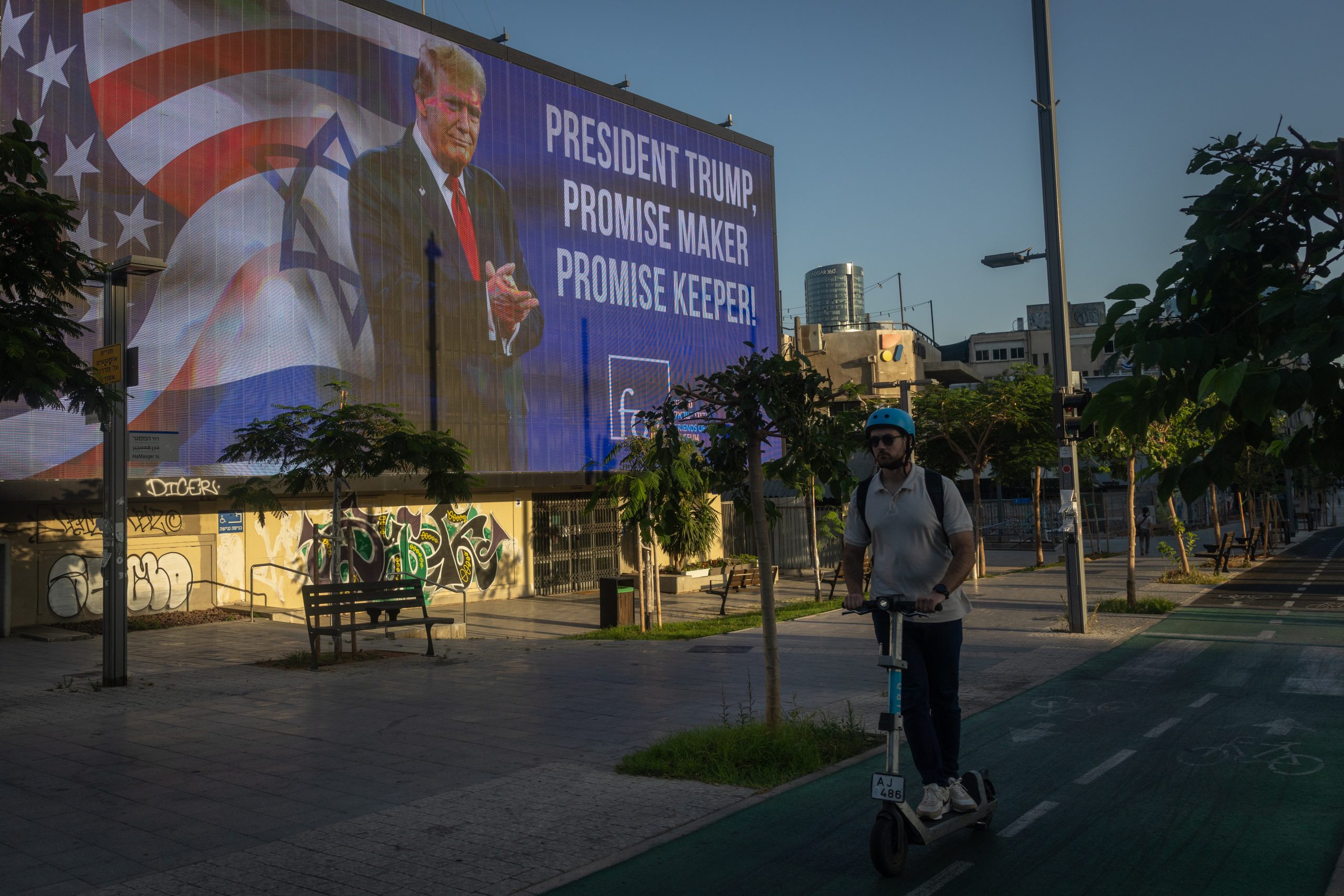 TEL AVIV, ISRAEL - JUNE 26: A man rides a scooter past a larger billboard depicting U.S. President Donald Trump on June 26, 2025 in Tel Aviv, Israel. As Israel's government touts its victory over Iran after 12 days of war, and a sense of normalcy returns to daily life here, Israelis are also recovering from a wave of aerial attacks that killed 28 people, caused an estimated $3 billion in damage, and tested the limits of its air-defense systems. (Photo by Chris McGrath/Getty Images)