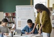 Girl assisting classmates in a language class with grammar rules in the background
