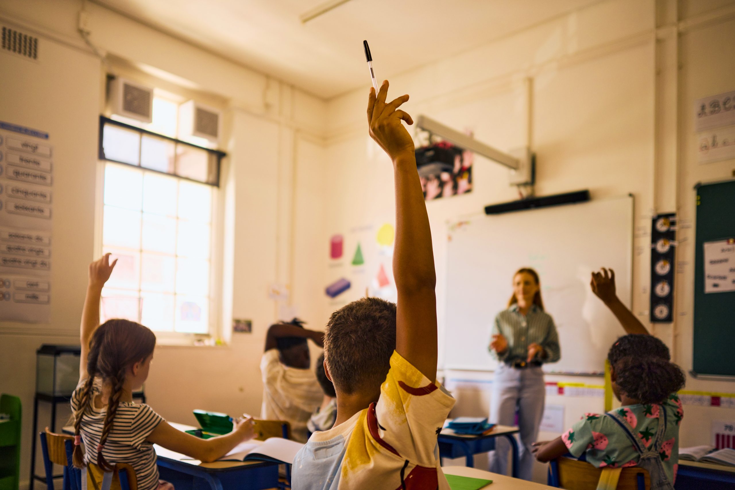 Diverse group of elementary school students actively participating in class, raising hands to answer teacher's question