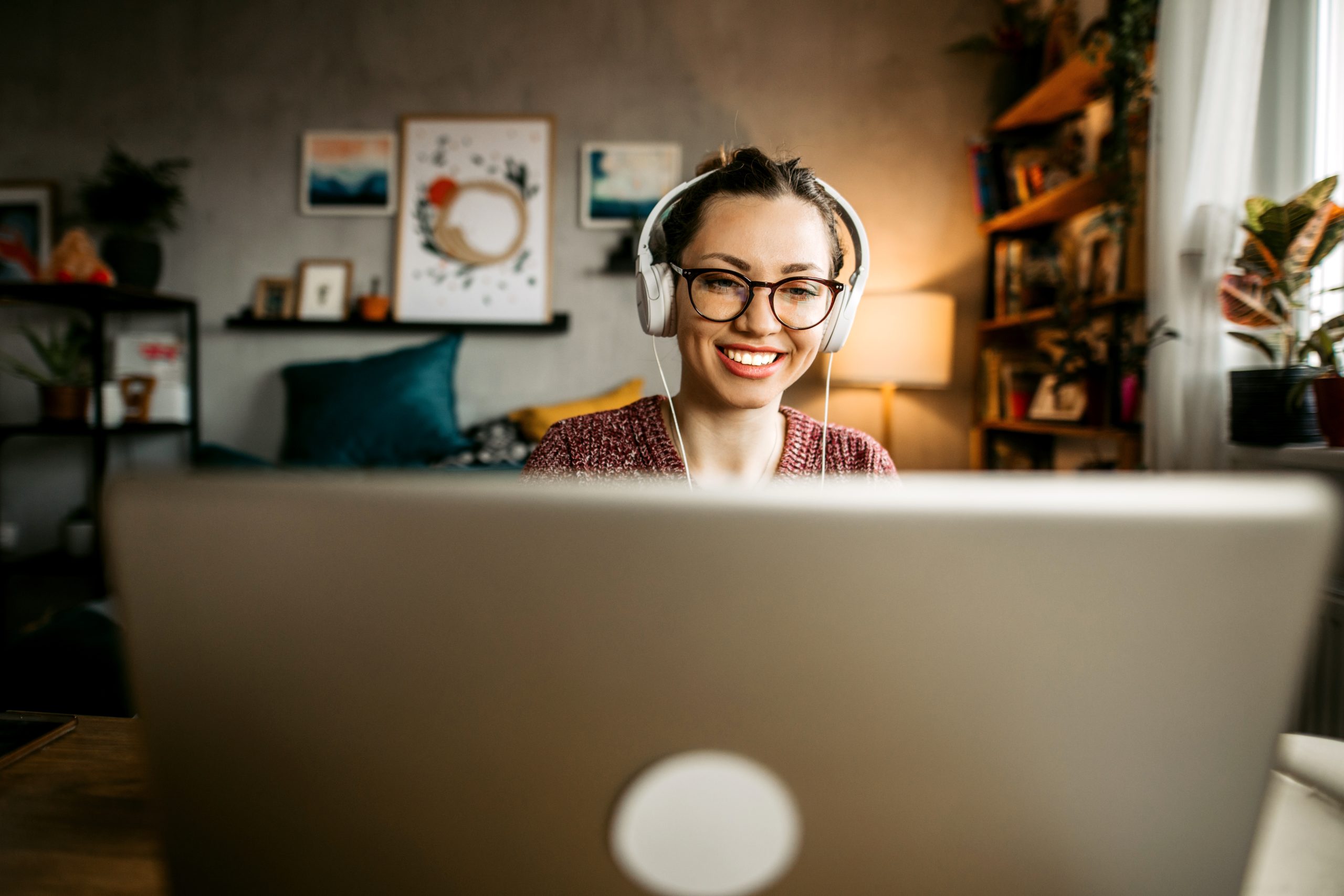 Young woman teaching online from her living room. Young woman wearing headphones while having a video call and looking at the camera.