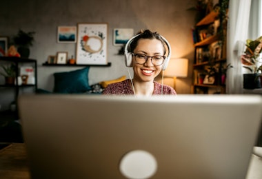 Young woman teaching online from her living room. Young woman wearing headphones while having a video call and looking at the camera.