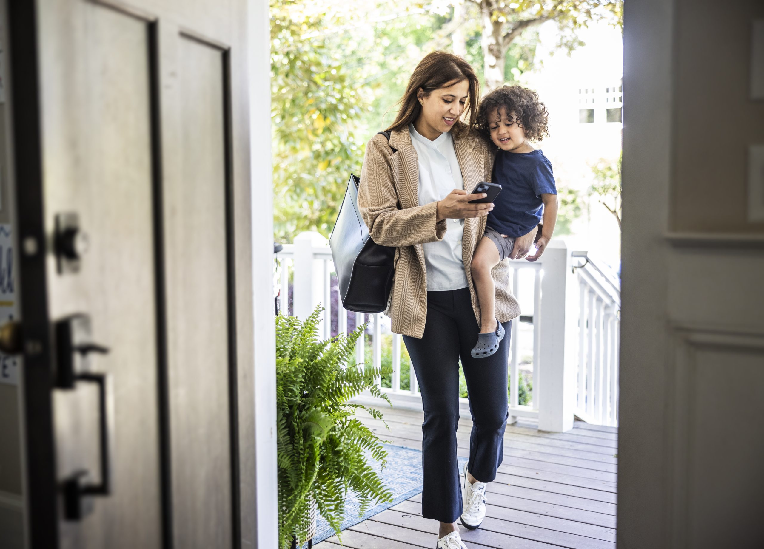 Mother walking through doorway with smartphone while holding toddler boy