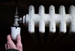 Detail with a hand checking the heat coming from a household radiator