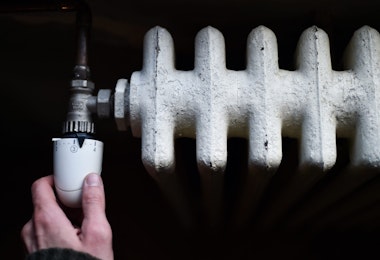 Detail with a hand checking the heat coming from a household radiator