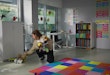 Tired young teacher clean playroom in kindergarten in evening. Female teacher collect toys from floor at nursery school classroom