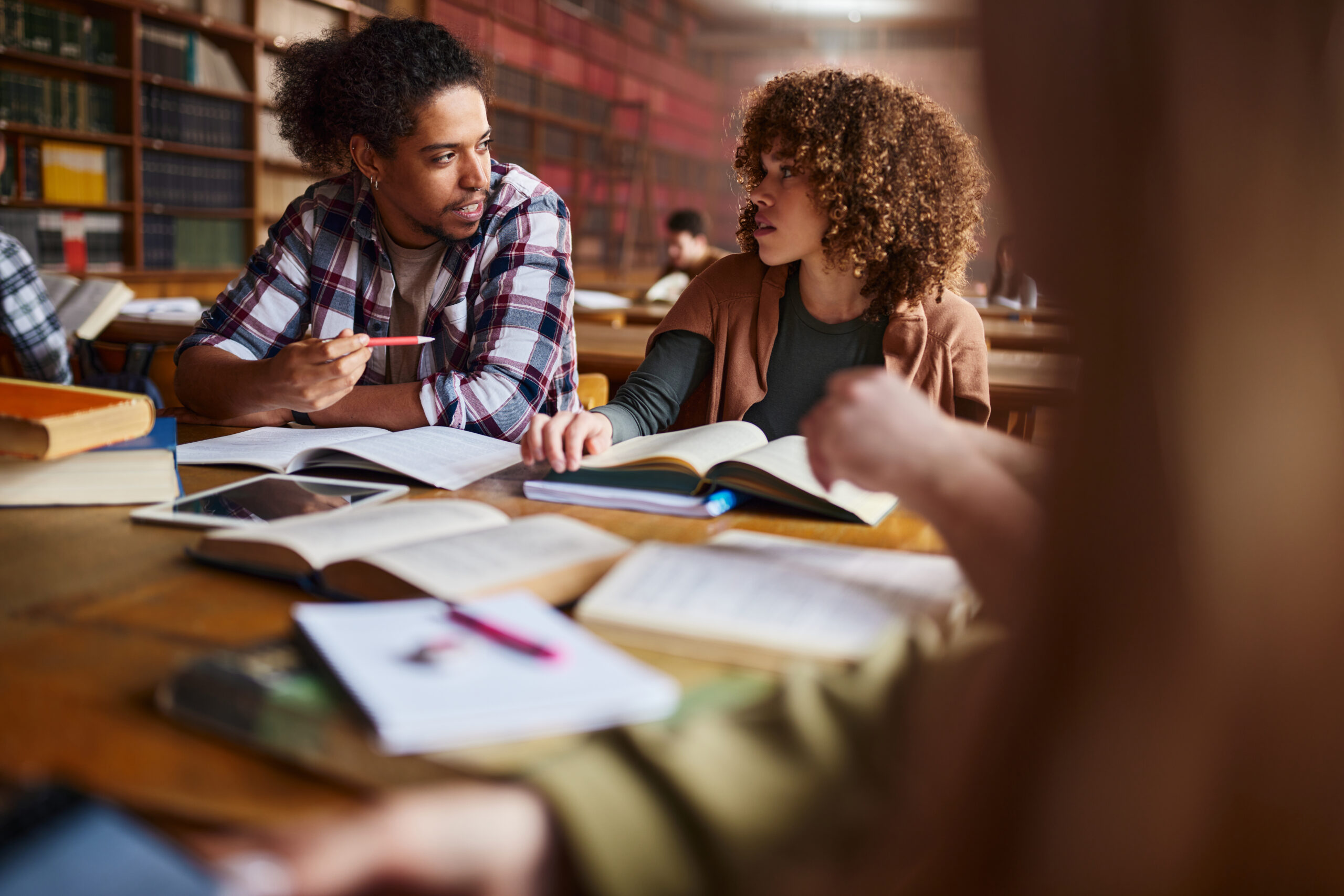 Diverse university friends communicating while learning for the exams in library.