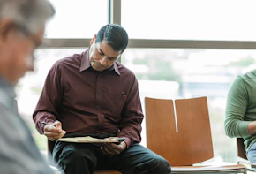 While in the lobby of the medical clinic, the mid adult man fills out his medical insurance information so he can be seen.