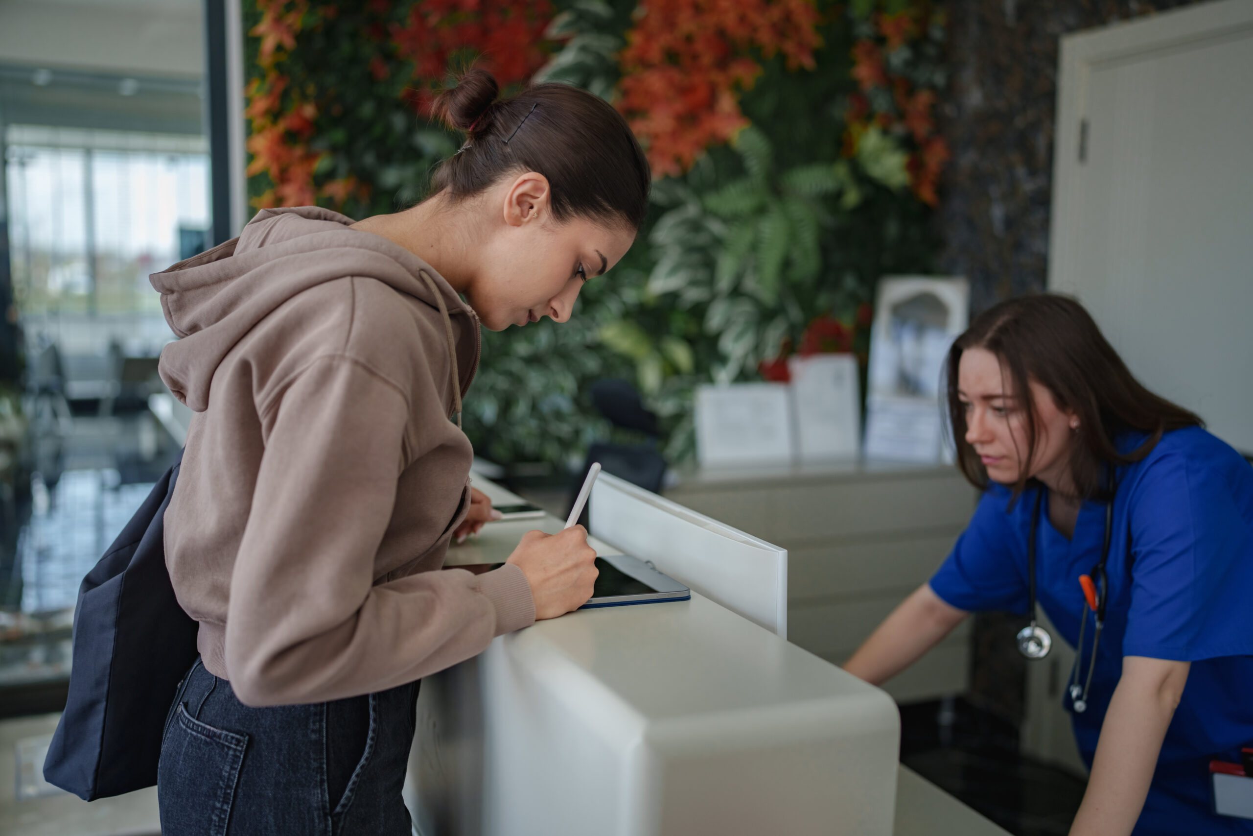 A woman at the clinic’s front desk using a digital tablet to complete a medical form. The scene reflects a modern healthcare setting with streamlined, paperless registration and patient-centered service.