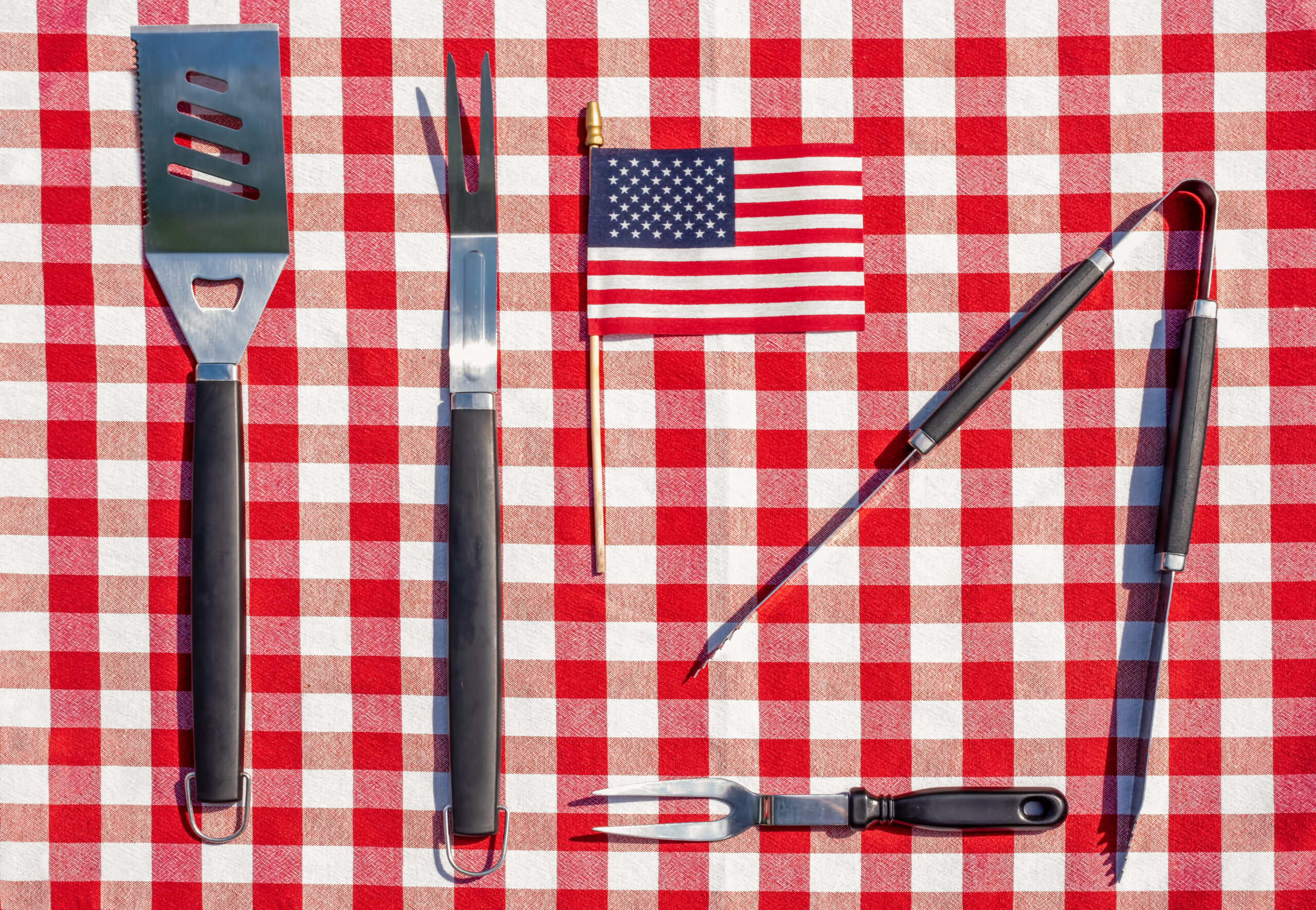 Metal grill tools and an american flag on a red and white checked picnic table